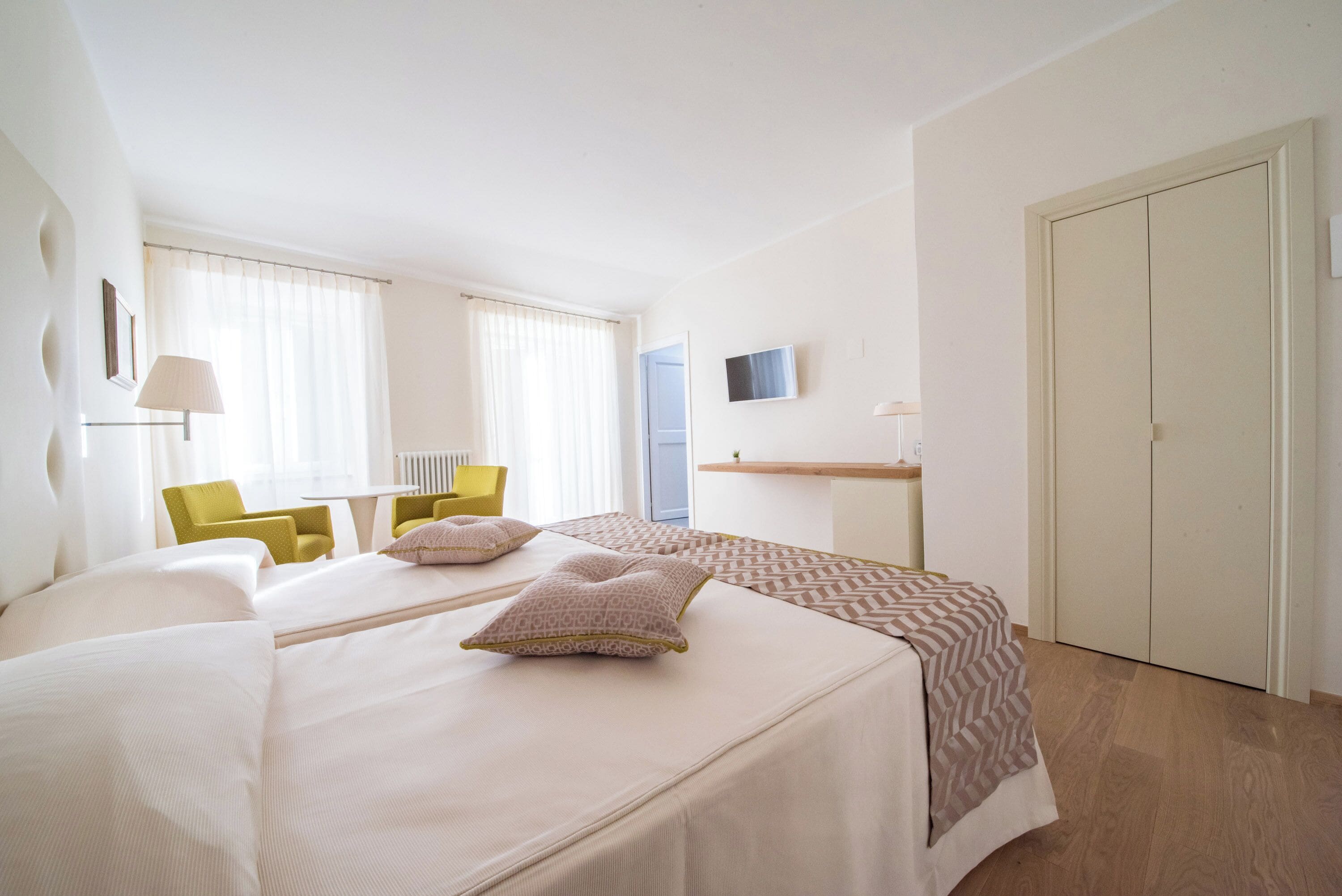 A hotel room with two beds, a desk, a chair, a TV, and a wardrobe.