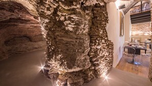 Un intérieur semblable à une grotte, avec un mur de roche naturelle, un plancher en bois et un coin repas comprenant des chaises transparentes et une table.