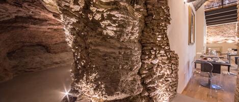 Ein höhlenähnlicher Innenraum mit einer natürlichen Felswand, Holzboden und einer Essecke mit transparenten Stühlen und einem Tisch.