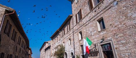 A narrow street lined with historic stone buildings, a flag, and a clear blue sky.