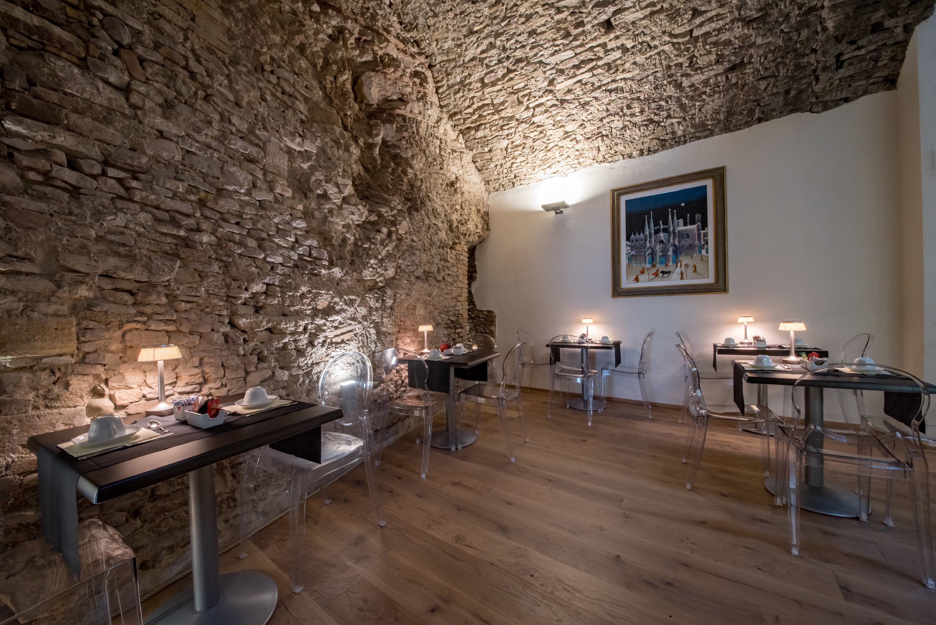A dining area with stone walls, clear chairs, and tables with lamps.