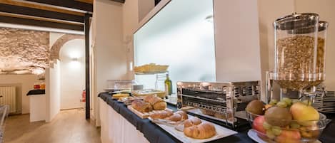 En morgenmadsbuffet med brød, kager, frugt og en kaffemaskine.