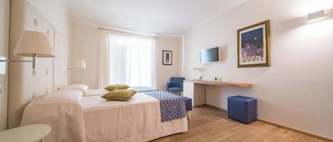 A hotel room with a bed, a desk, a chair, a TV, and a window with curtains.