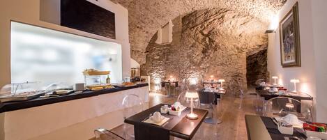 A restaurant with a rustic stone ceiling, clear glass tables, and modern lighting.