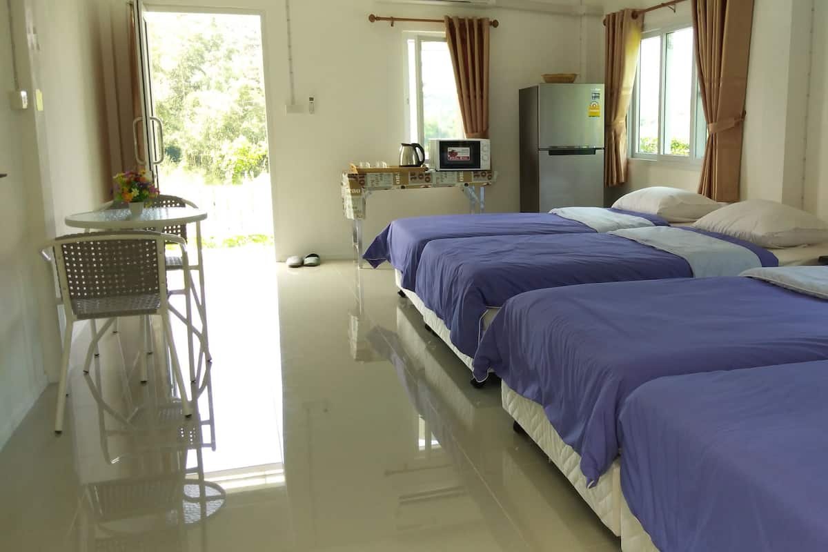 Een hotelkamer met drie bedden, een kleine tafel met stoelen, een koelkast en een raam met gordijnen.