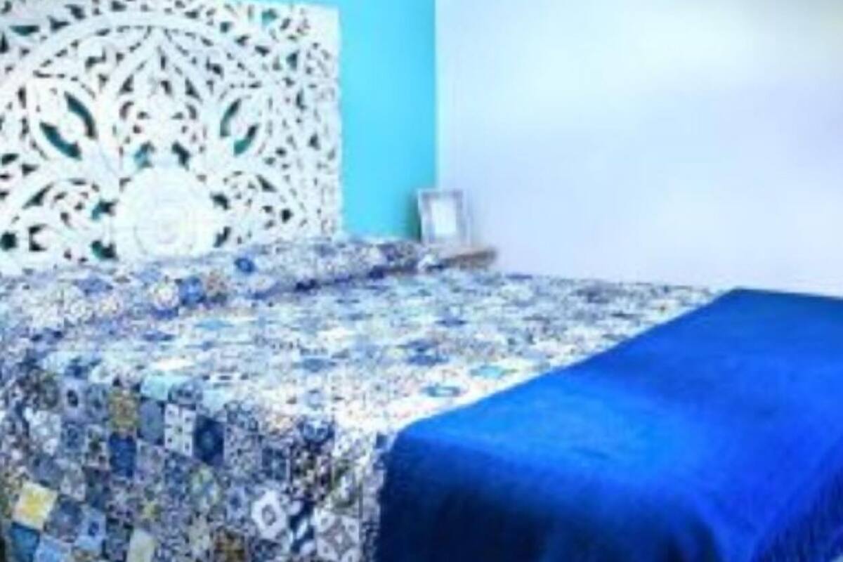 A bed with a blue blanket and a patterned quilt.