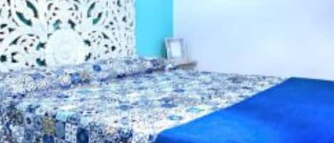 A bed with a blue blanket and a patterned quilt.