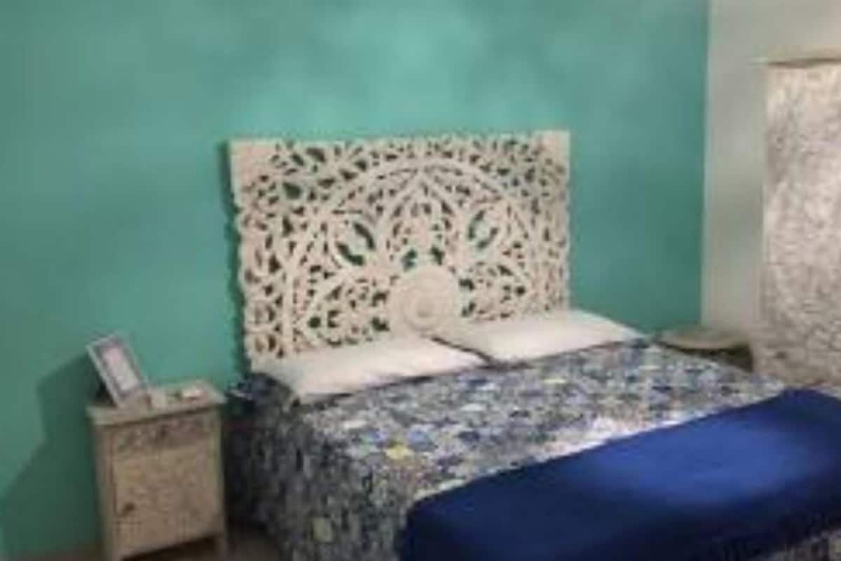 A bedroom with a patterned bedspread, a decorative headboard, and a wardrobe.