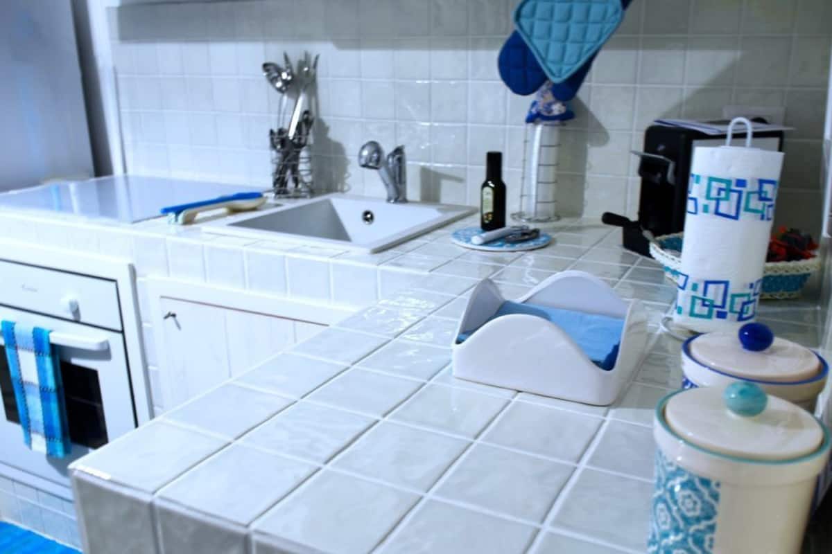 A kitchen with white tiles, a sink, a stove, and various kitchen items on the counter.