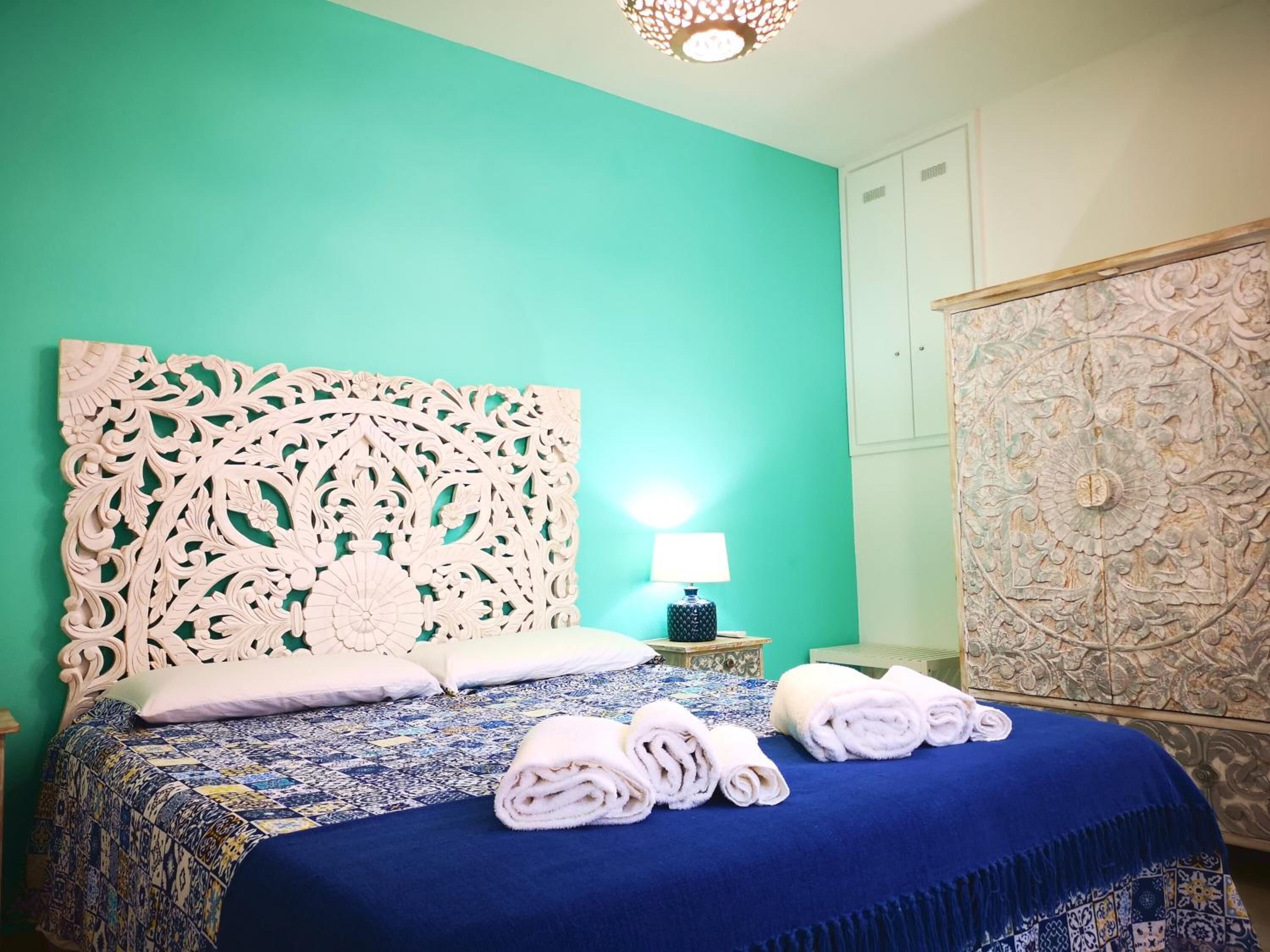 A bedroom with a large bed, a decorative headboard, a nightstand with a lamp, and a wardrobe with intricate designs.