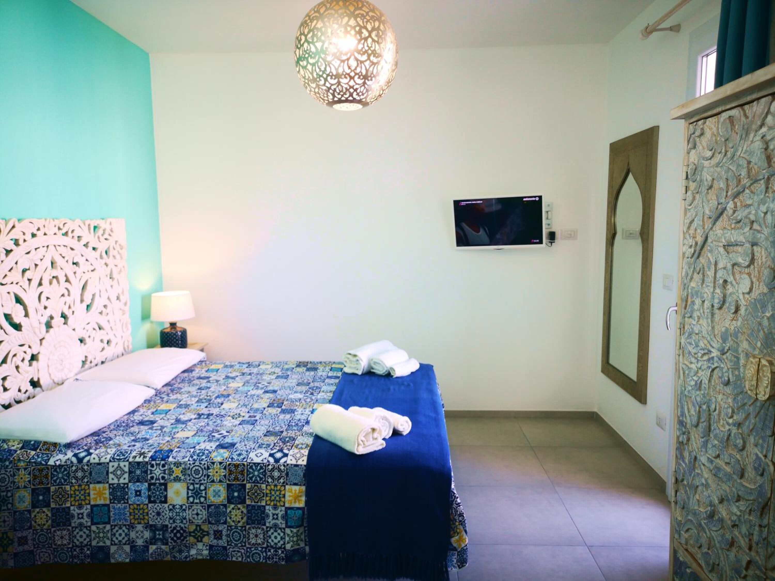 A bedroom with a patterned bedspread, a decorative headboard, a wall-mounted TV, and a mirror.