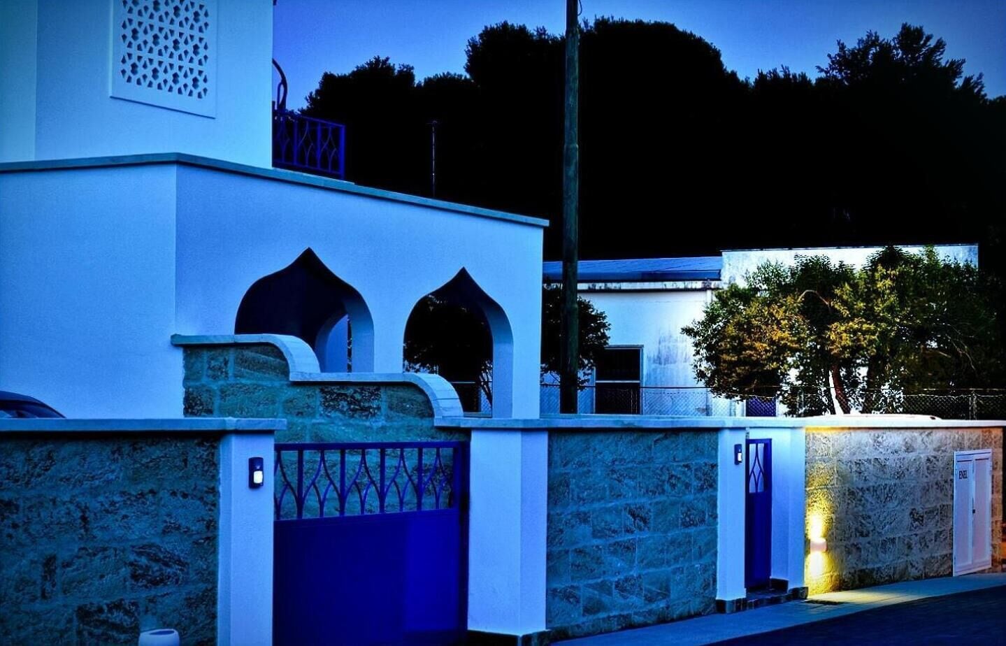 Un bâtiment à la façade en pierre, doté d’une entrée sécurisée par un portail et d’un éclairage extérieur bleu.