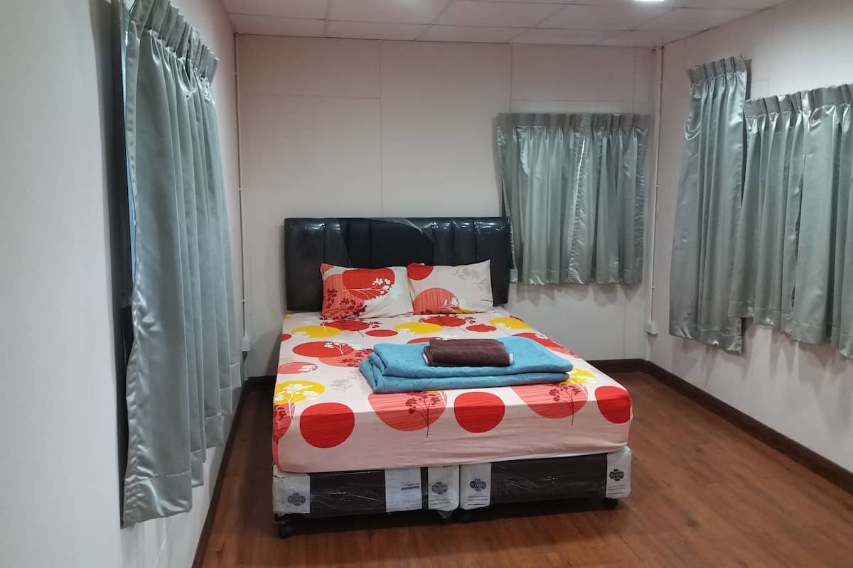 A neatly made bed with a floral-patterned bedspread, a black headboard, and a brown pillow.