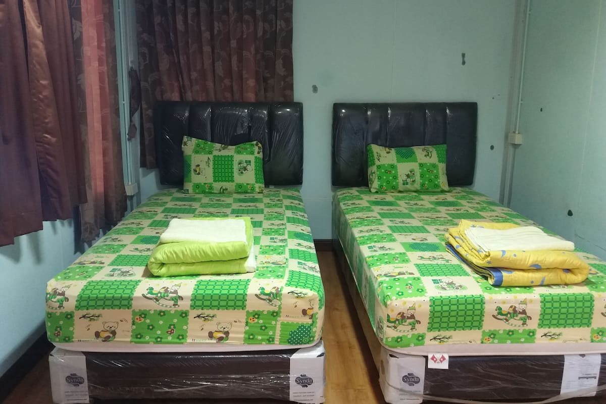 Two single beds with green and white checkered bedding, black headboards, and a window with curtains.