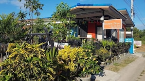 A building with a covered outdoor area, surrounded by various plants and trees. - Nakhonyok Homestay (Nakhon Nayok)