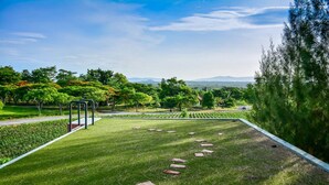 Une pelouse bien entretenue, agrémentée de pas japonais et d’une structure métallique, le tout entouré d’arbres et sous un ciel dégagé.