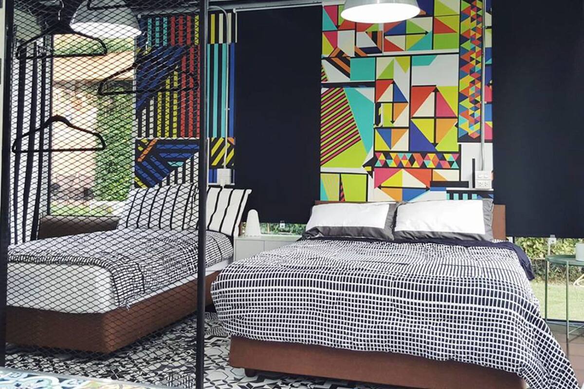 Een moderne slaapkamer met een bed, een stoel en een kleurrijk geometrisch ontwerp op de muur.