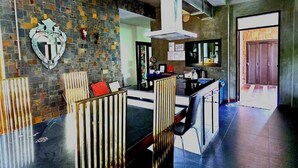 Une cuisine moderne avec un mur de crédence en pierre, un coin repas avec une table noire et des chaises à rayures, et un îlot de cuisine bien visible.