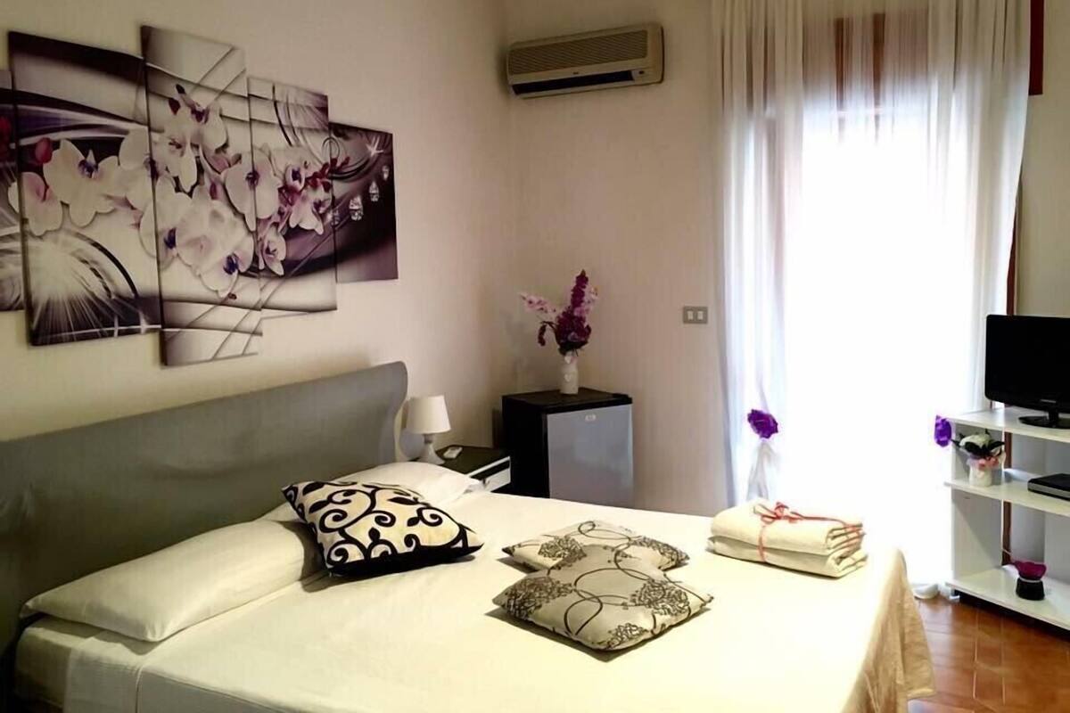 Ein Hotelzimmer mit Bett, Fernseher, Schreibtisch und einem Fenster mit Vorhängen.