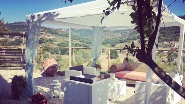 An outdoor seating area with white wicker furniture, a covered section, and a view of the countryside. - Villa Rosa (Agropoli)