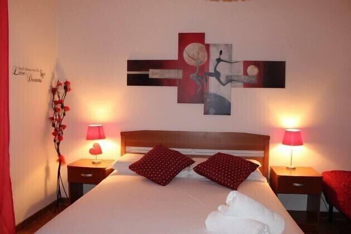 Ein Hotelzimmer mit einem Bett, zwei Nachttischen mit Lampen, einem Wandbild und einer Zimmerpflanze.