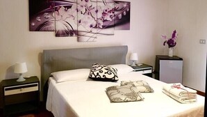 A hotel room with a bed, a nightstand, a lamp, a decorative pillow, a vase with flowers, and a wall-mounted air conditioner. - Villa Rosa (Agropoli)