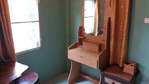 A room with a wooden vanity, a mirror, a window with curtains, and a small table.