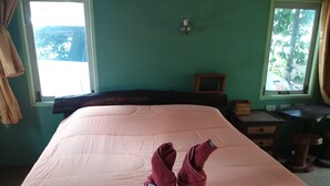 A room with a large bed, a desk, and a window with a view of greenery.