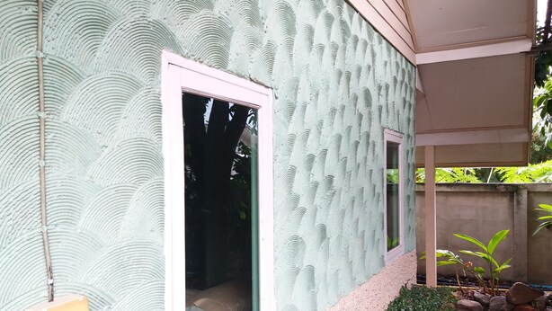 A building exterior with a textured wall, a window, and a small garden area with rocks and plants.