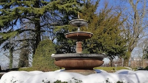 Une fontaine en pierre à plusieurs niveaux, entourée de neige, avec des arbres en arrière-plan.