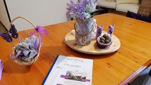 Une table en bois avec une brochure, un panier décoré de rubans violets, un vase rempli de fleurs et des biscuits en forme de hibou.