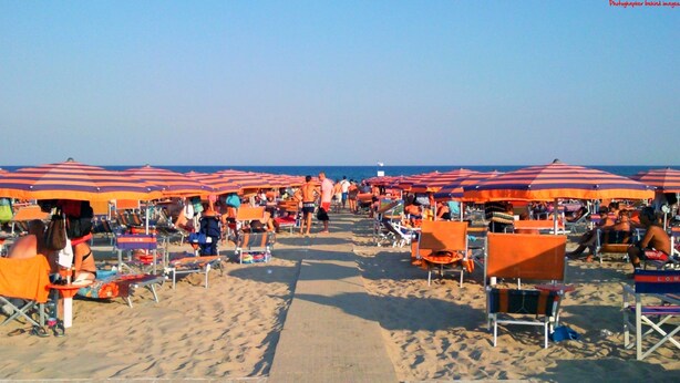 A beach with rows of orange and red striped umbrellas and beach chairs. - B&B Villa Giada (Ginosa)