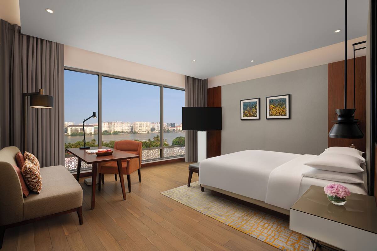 Ein Hotelzimmer mit großem Fenster, einem Bett, einem Schreibtisch und einem Sessel.