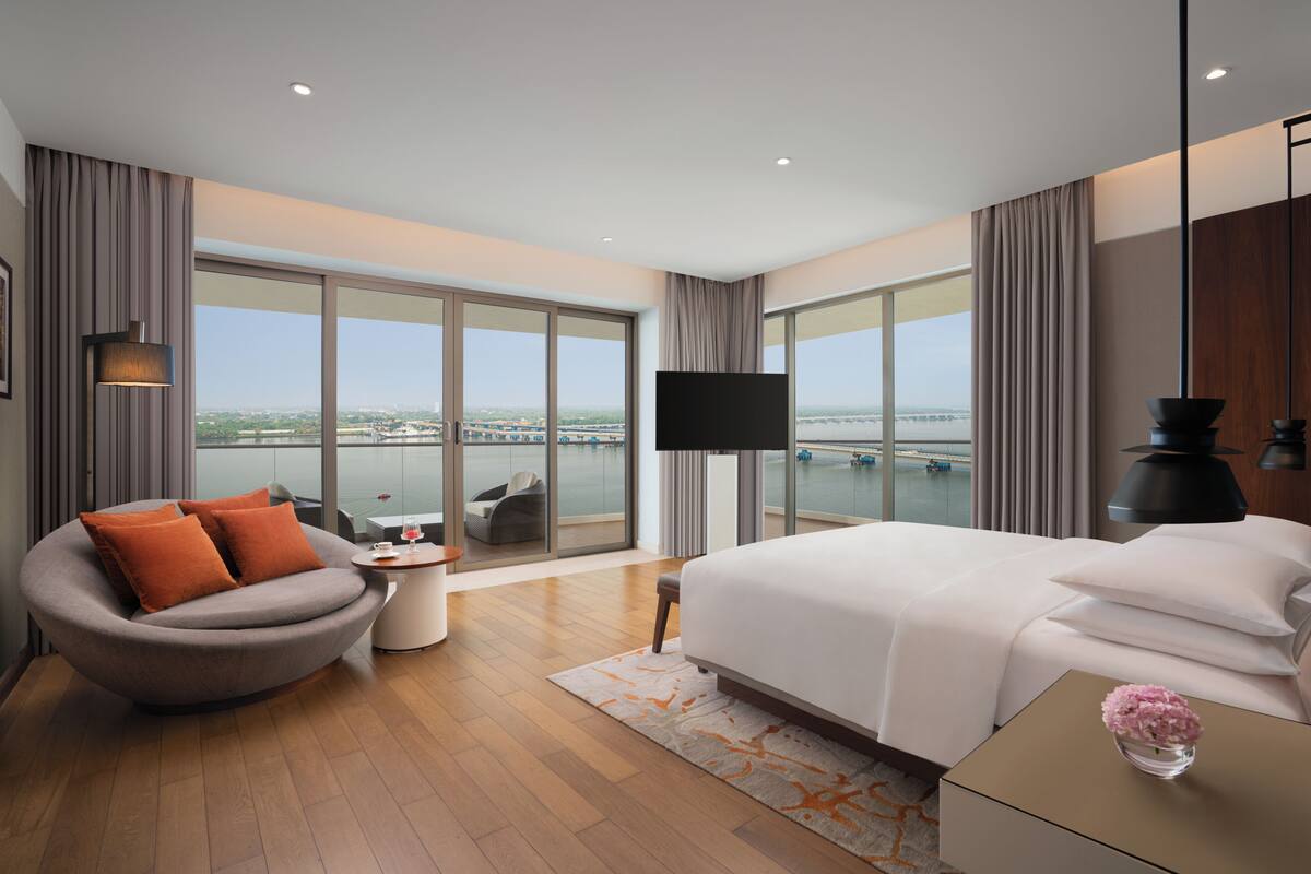 Ein modernes Hotelzimmer mit einem großen Bett, einer gebogenen Couch, einem Flachbildfernseher und Blick auf ein Gewässer.