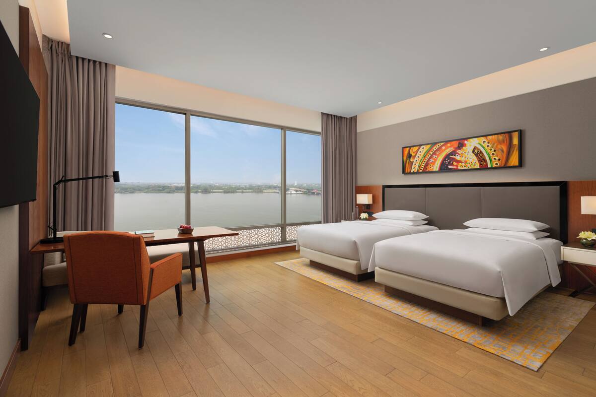 Ein Hotelzimmer mit großem Fenster, zwei Betten, einem Schreibtisch und einem Stuhl.