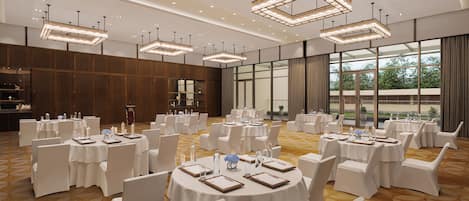 Un amplio salón de banquetes con mesas redondas, sillas blancas e iluminación colgante moderna.