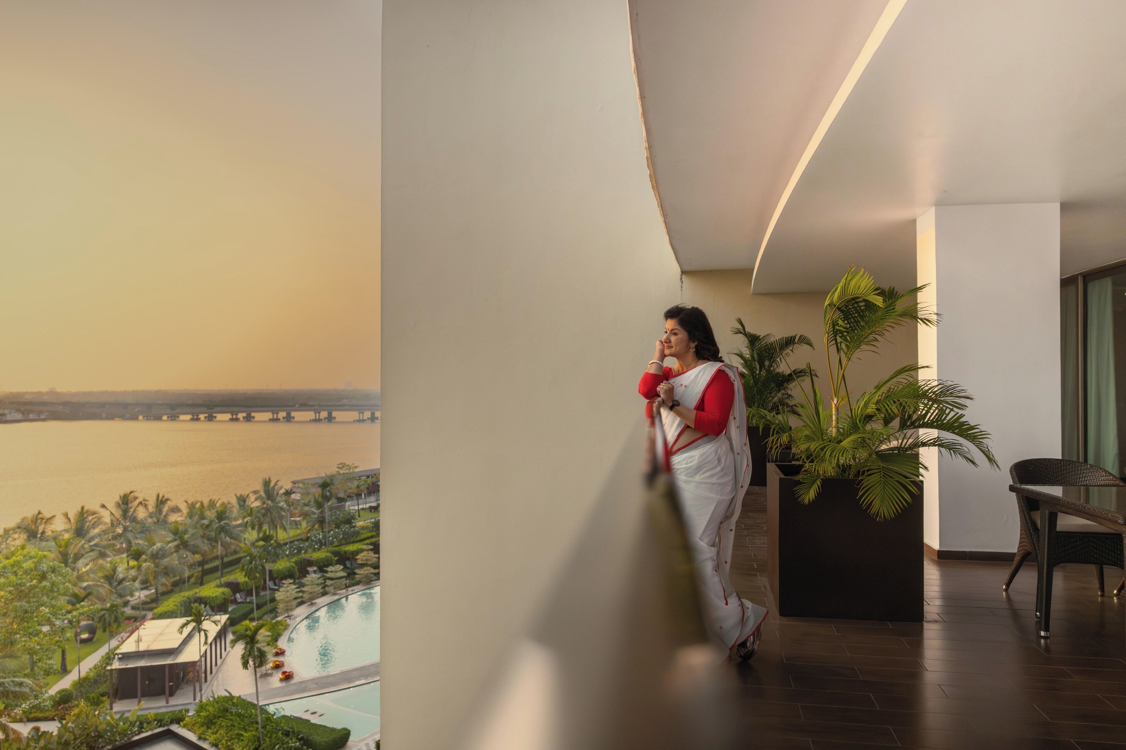 A person in a white and red outfit standing on a balcony with a view of a body of water and a bridge.