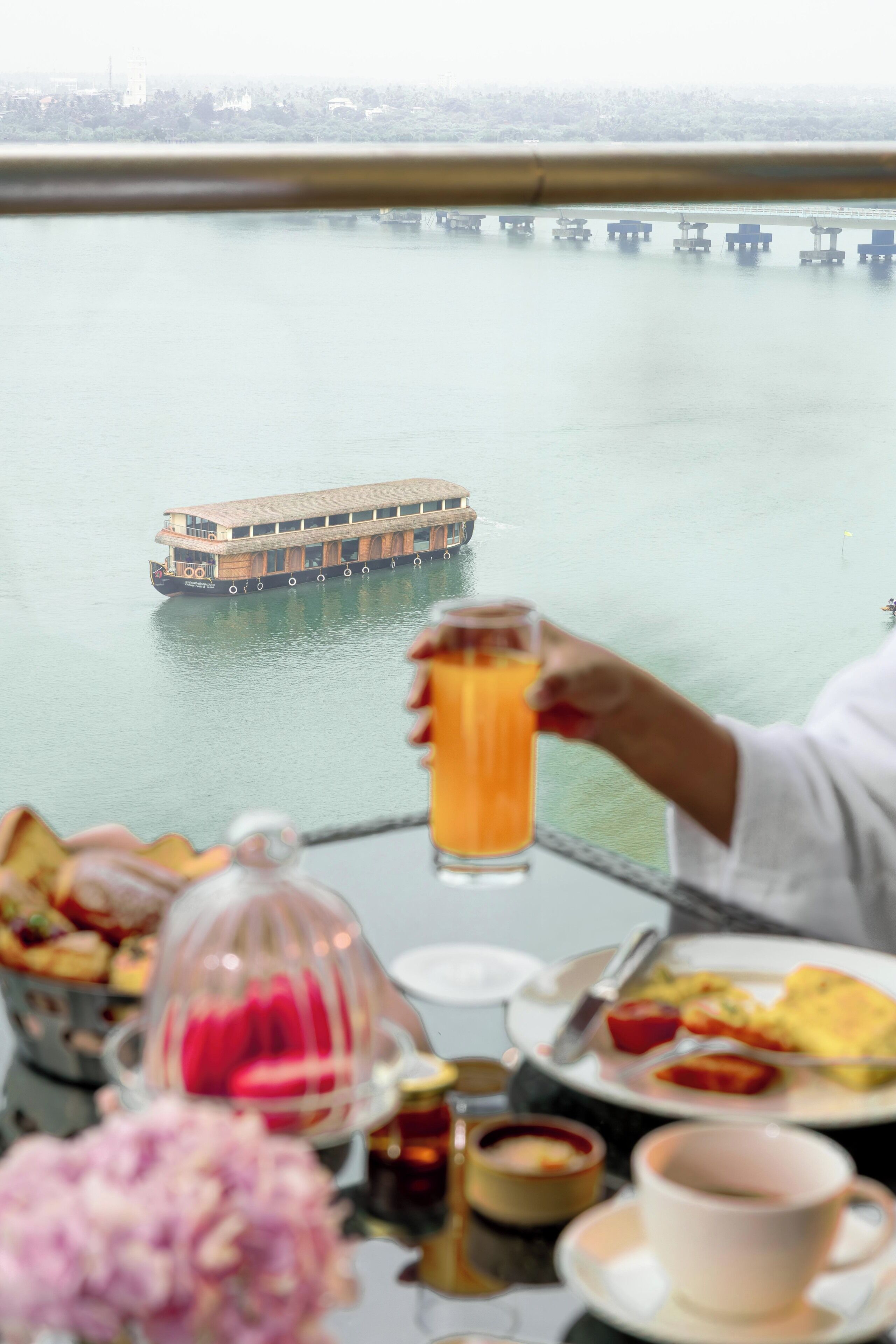 A table with breakfast items, a glass of orange juice, and a view of a river with a boat.