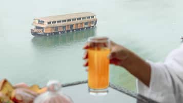 A table with breakfast items, a glass of orange juice, and a view of a river with a boat.