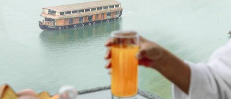 Una mesa con alimentos para el desayuno, un vaso de jugo de naranja y vistas a un río con un barco.