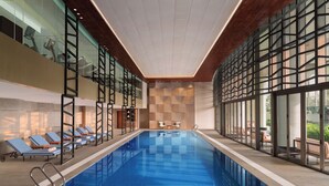 Ein Hallenbad mit Liegestühlen, einer karierten Wand und großen Fenstern.