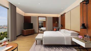 A modern hotel room with a large bed, a desk, a TV, and a view of the city.