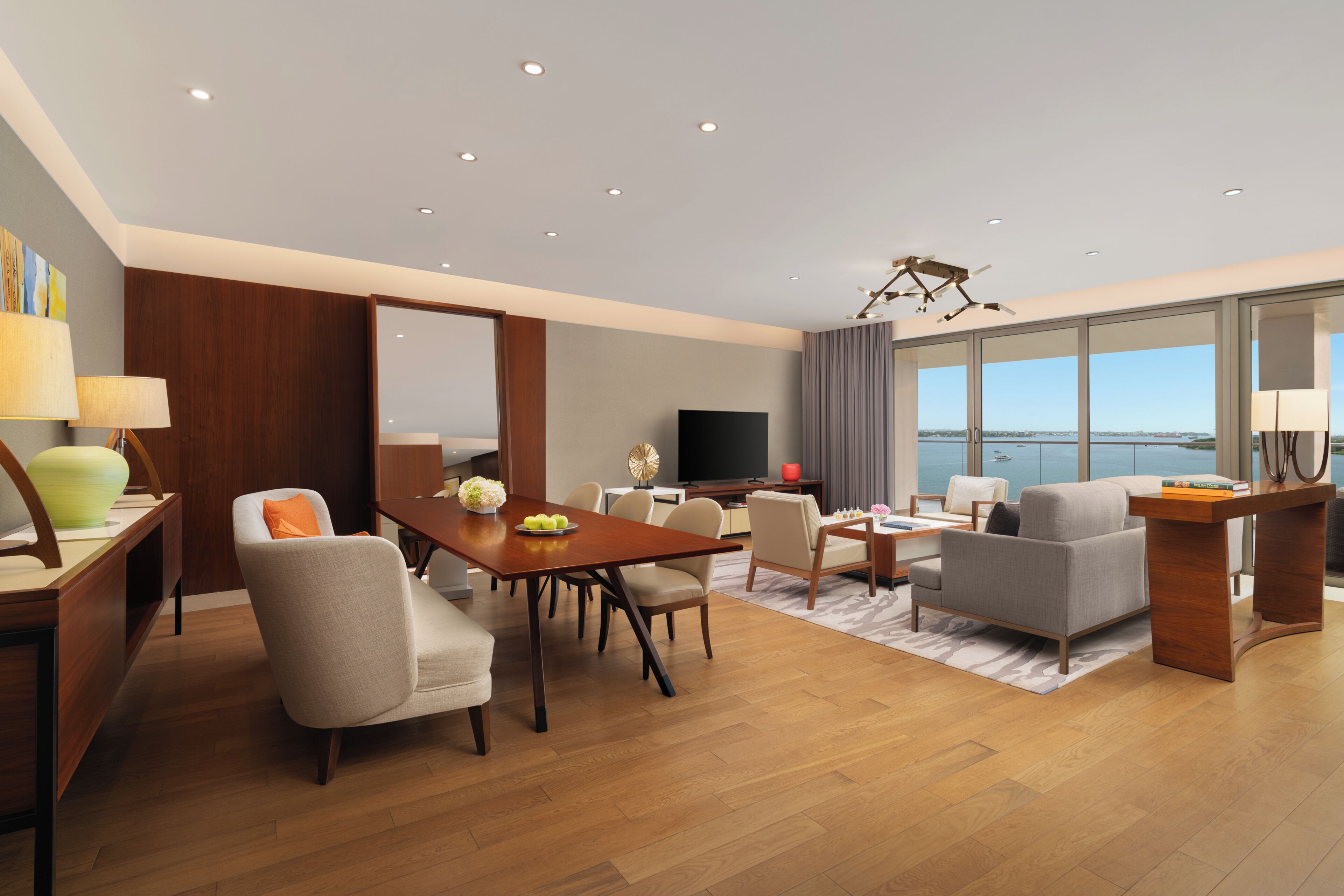 A modern living room with a dining area, a flat-screen TV, and a large window with a view.