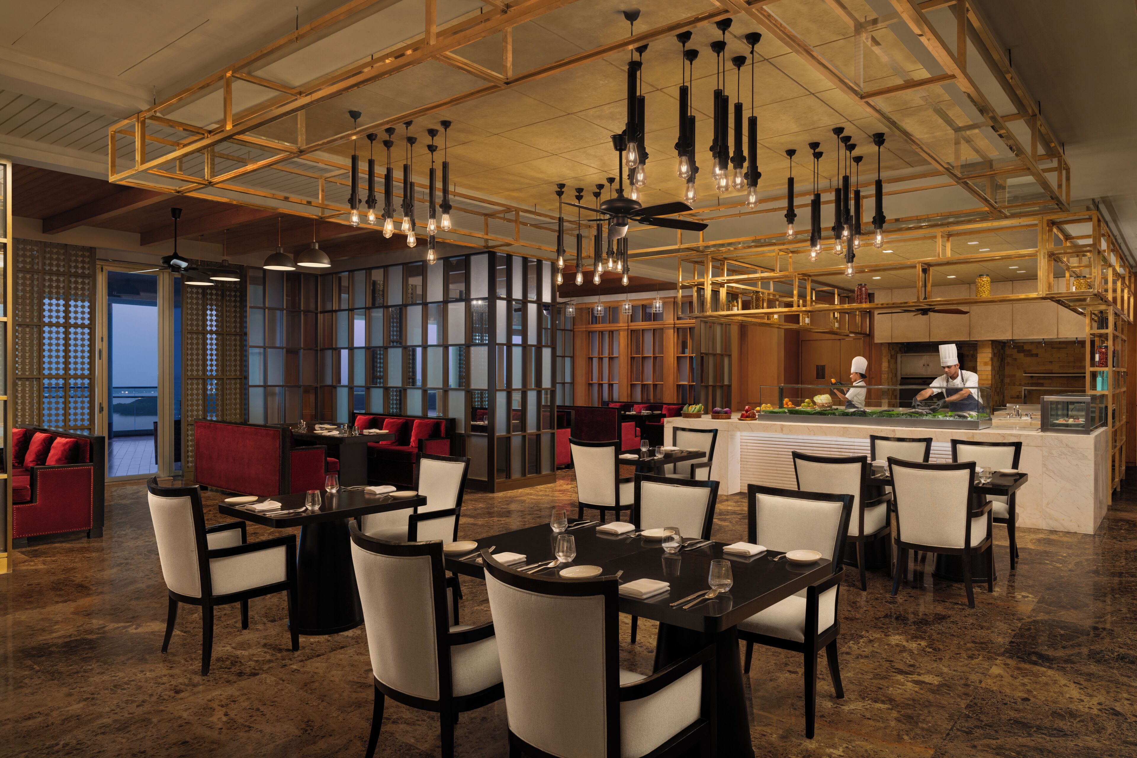 A restaurant with high ceilings, hanging light fixtures, and a view of the kitchen.