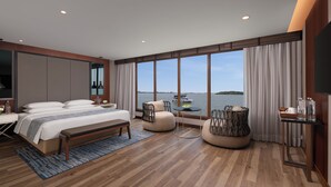 Ein modernes Hotelzimmer mit einem großen Bett, einer Sitzecke, einem kleinen Tisch und Blick auf das Wasser.