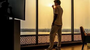 A person standing by a large window overlooking a body of water with a cityscape in the distance.