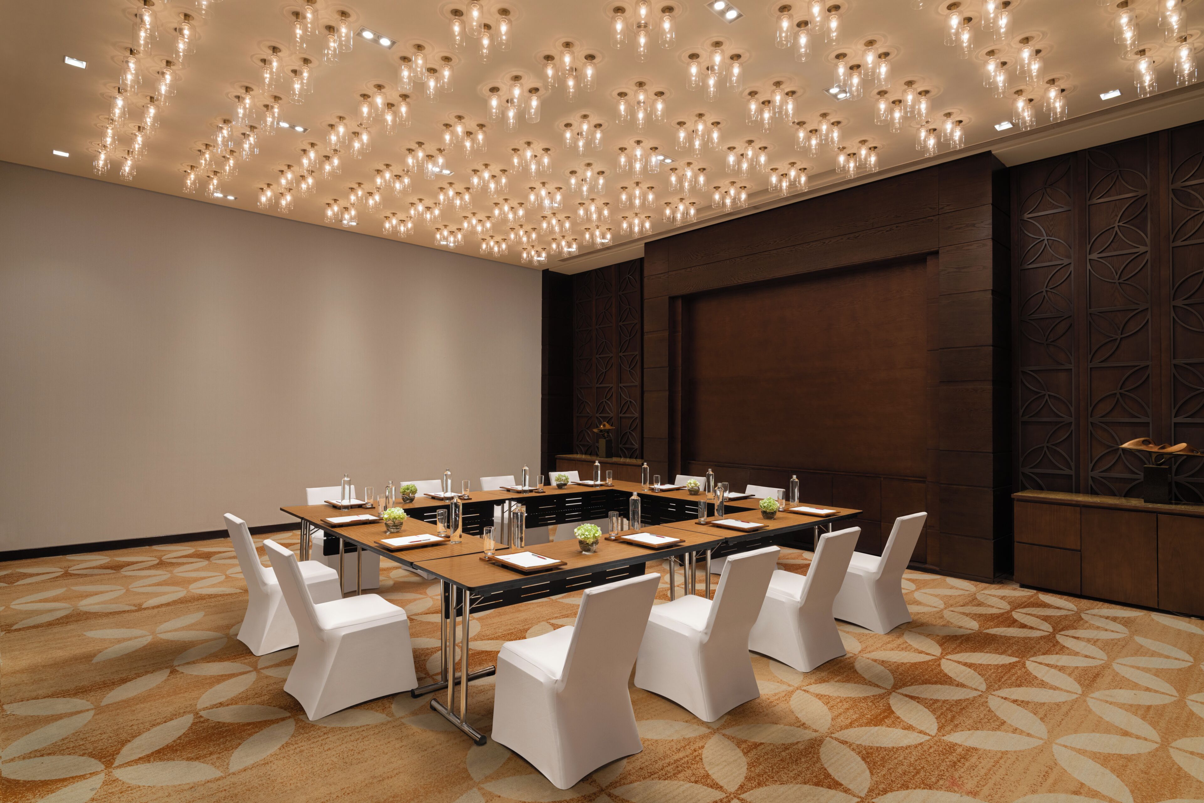 A conference room with a long table, white chairs, and a patterned carpet.