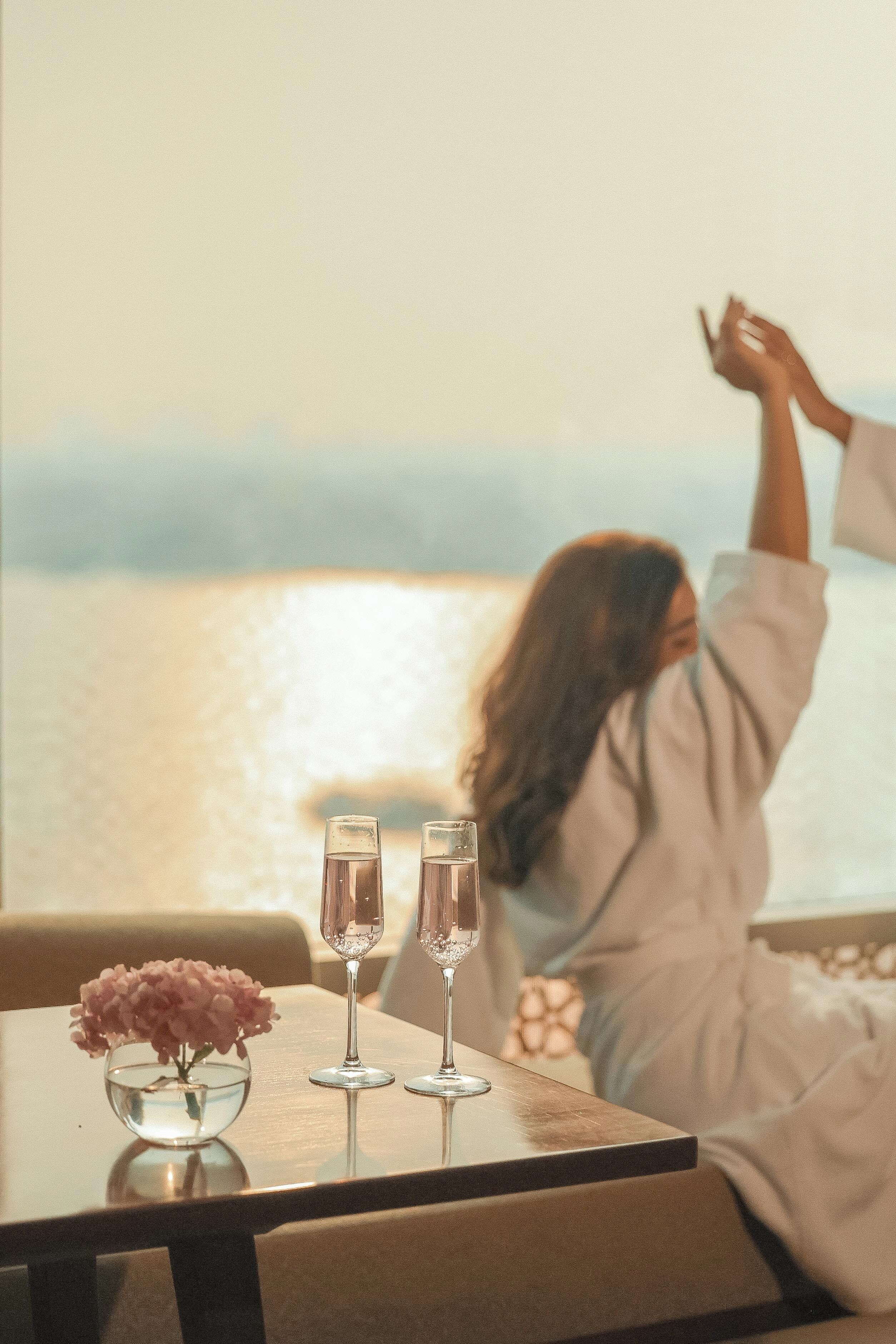A table with two glasses and a vase of flowers, overlooking a body of water.