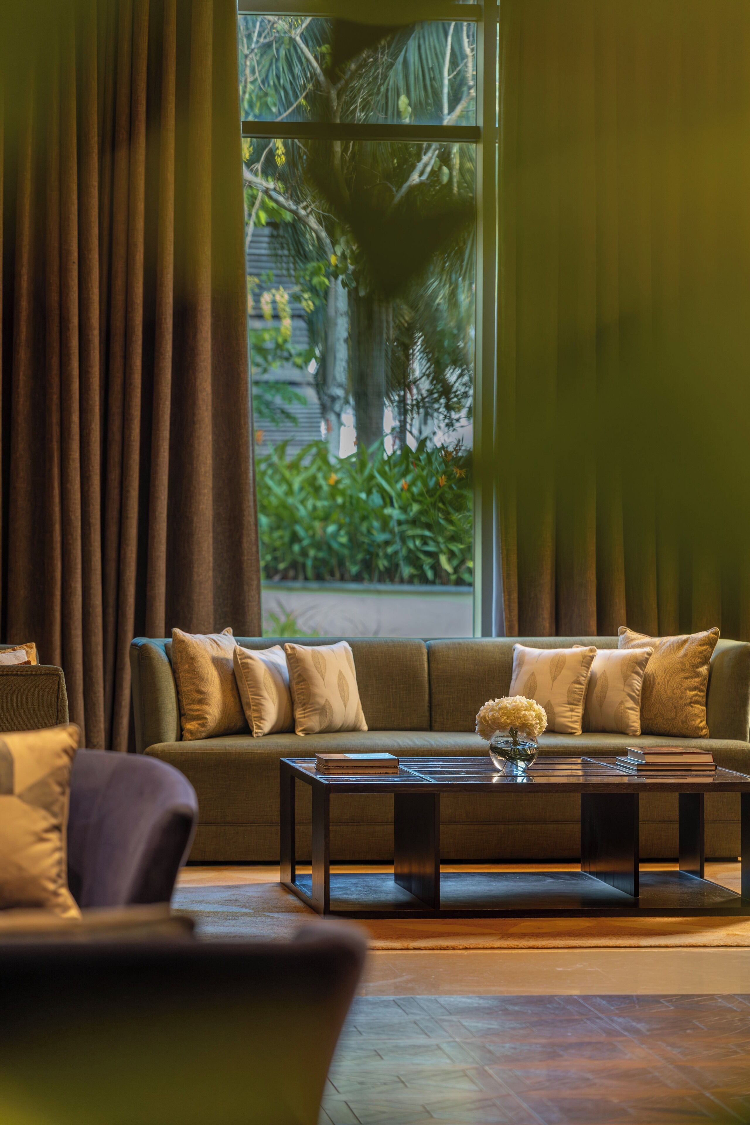 A modern living room with a sofa, a coffee table, and a view of greenery outside.