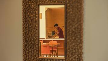 A kitchen with a person cooking, a wooden cabinet, and a small dining area with a chair.